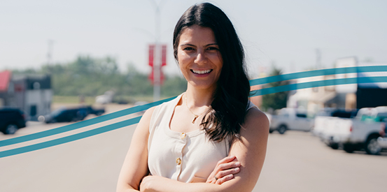 A smiling individual with arms crossed and the blurry image of a town street behind them.