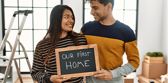 Young latin couple smiling happy holding our first home blackboard at new house.