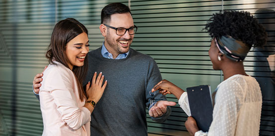 Happy couple buying their new home and receiving keys from real estate agent. 